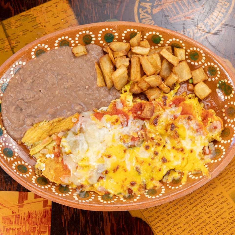 A Mexican breakfast plate with huevos rancheros, refried beans, and home fries on a decorative plate.