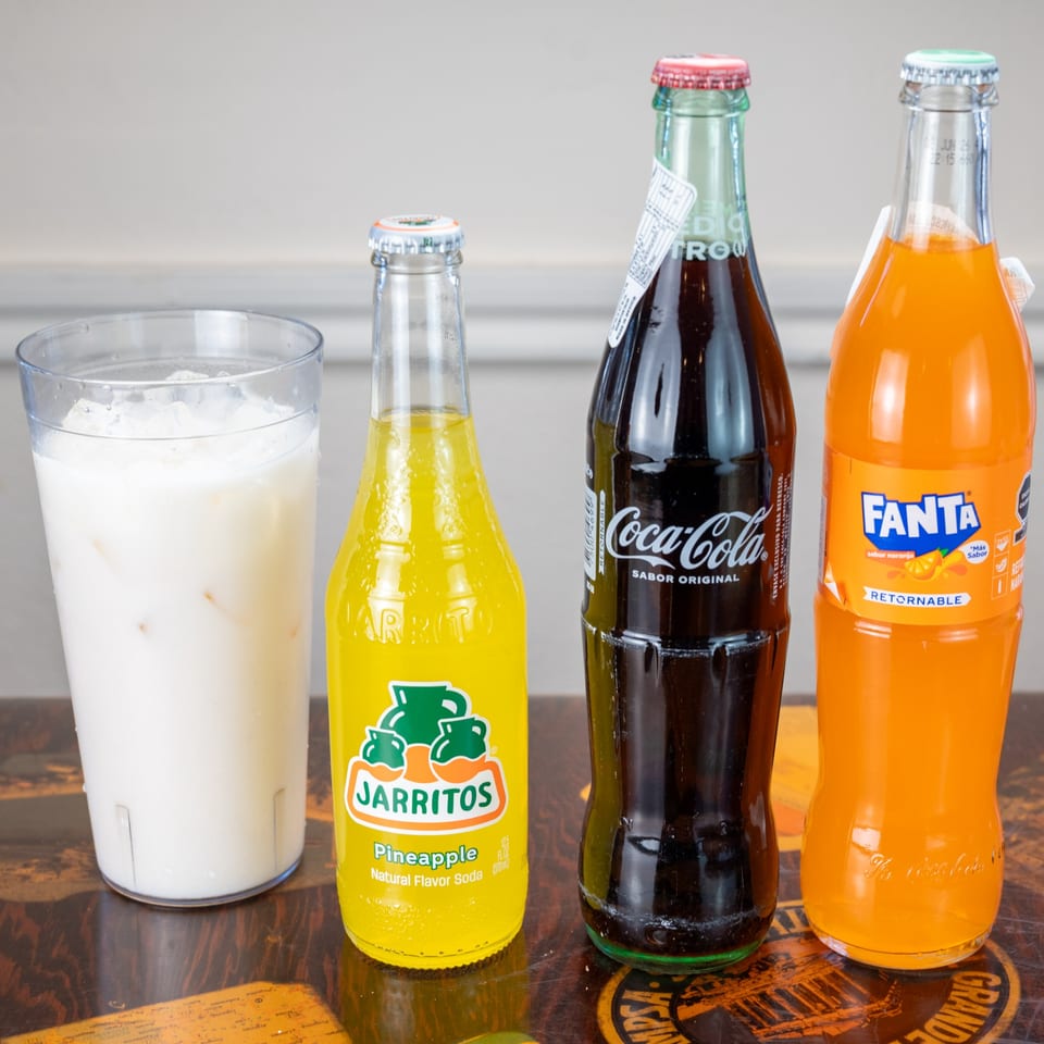 Horchata, Jarritos pineapple soda, Mexican Coca-Cola, and Fanta orange soda on a table.