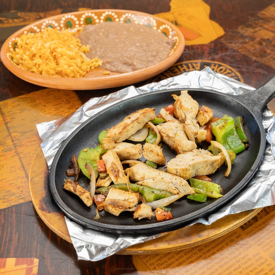Sizzling chicken fajitas with peppers and onions, alongside rice and refried beans.